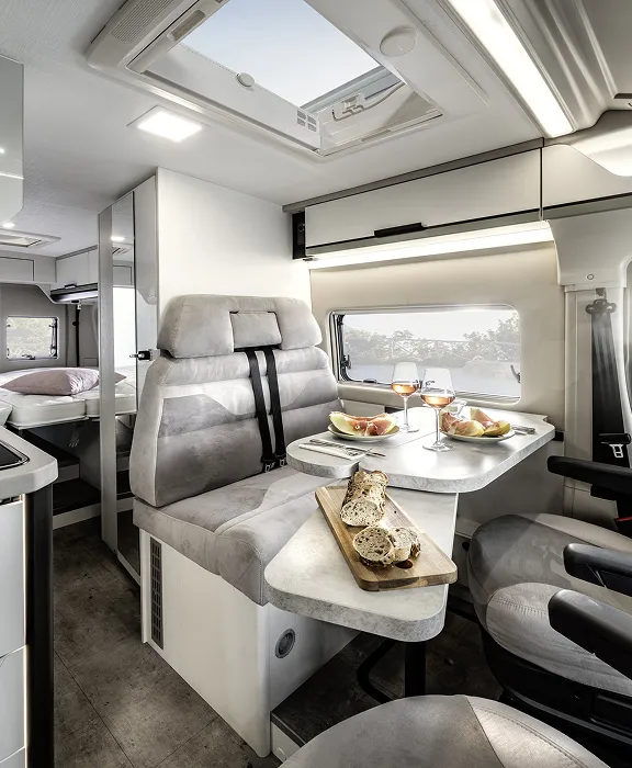 Karmann-Mobil Campingbus steht auf felsigem Küstenabschnitt mit Blick auf das Meer unter bewölktem Himmel und leichtem Sonnenlicht.